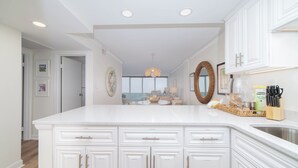A spacious kitchen with white cabinetry, a large island, and a view to the dining area.