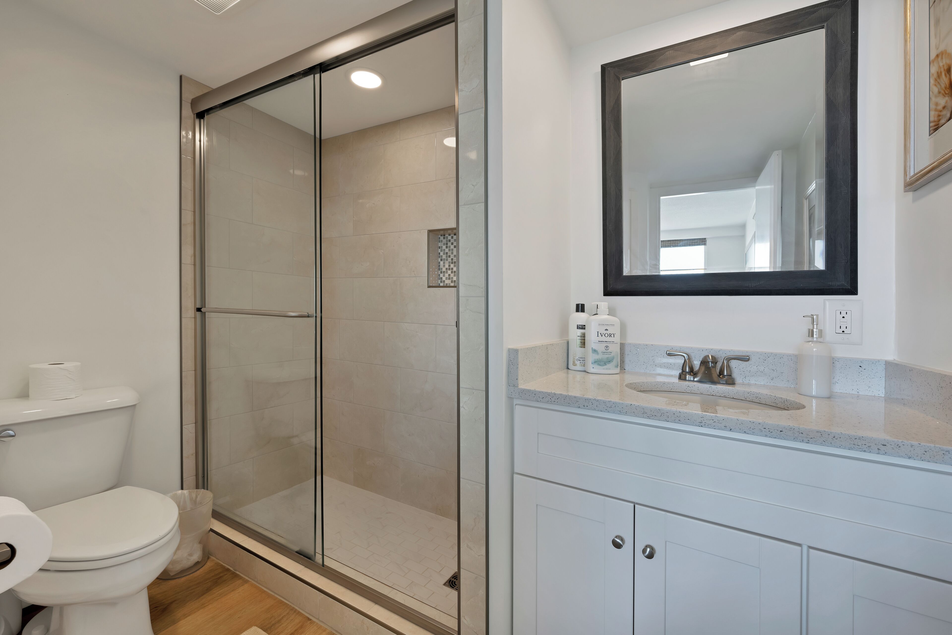 Un baño moderno con cabina de ducha de vidrio, inodoro blanco y tocador con espejo.