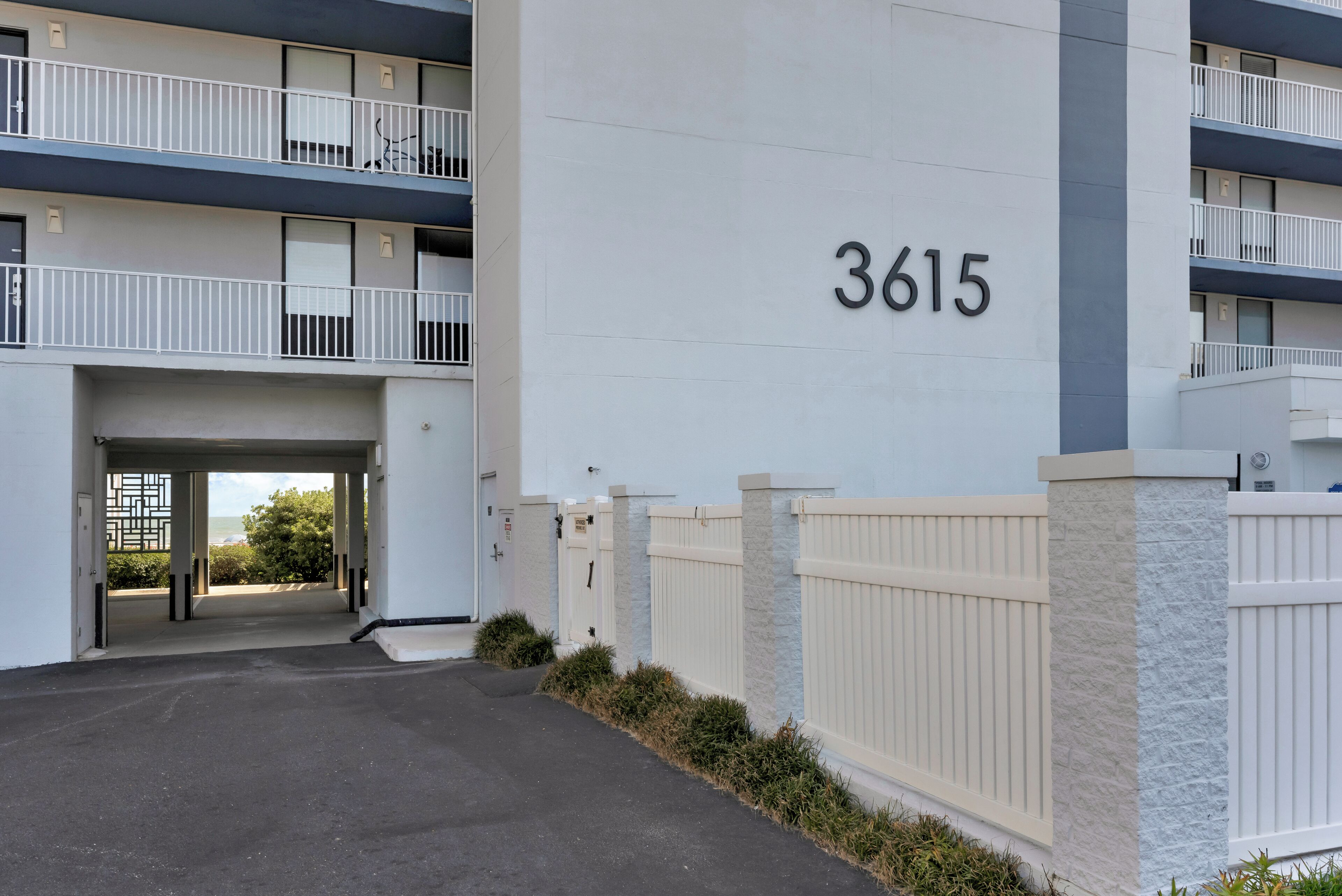 A modern building with a large number '3615' on the facade, a gated entrance, and a covered walkway leading to a balcony.