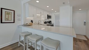 A modern kitchen with white cabinets, a large island with bar stools, and a framed picture on the wall.