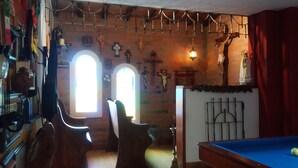 A room with a pool table, two arched windows, and various religious decorations on the walls.