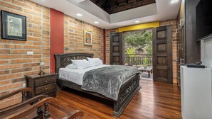 A bedroom with a brick wall, a wooden bed, a nightstand, and a view of the outdoors.