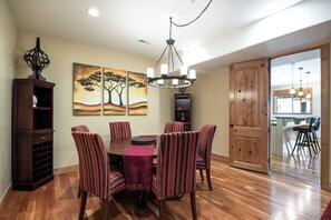 Un coin repas avec une table en bois, six chaises à rayures et un lustre. Deux tableaux ornent le mur, et un buffet en bois surmonté d’un globe terrestre se trouve dans la pièce.