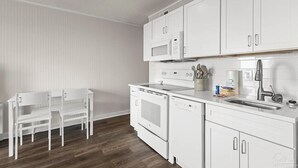 Una cucina moderna con mobili bianchi, forno a microonde integrato, forno e lavastoviglie. C'è un tavolo da pranzo bianco con sedie.