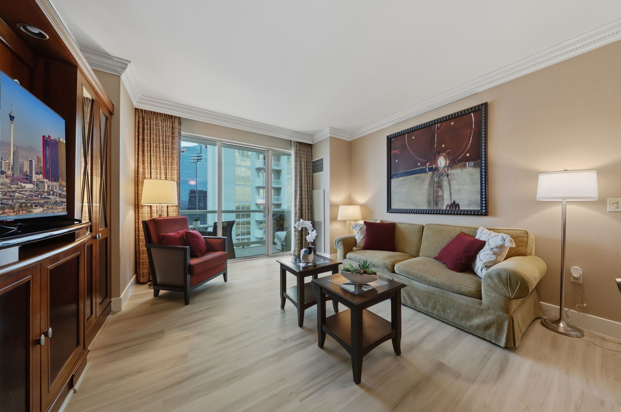 Ein Hotelzimmer mit großem Fernseher, einer Couch, einem Sessel, einem Couchtisch und einem Bild an der Wand.