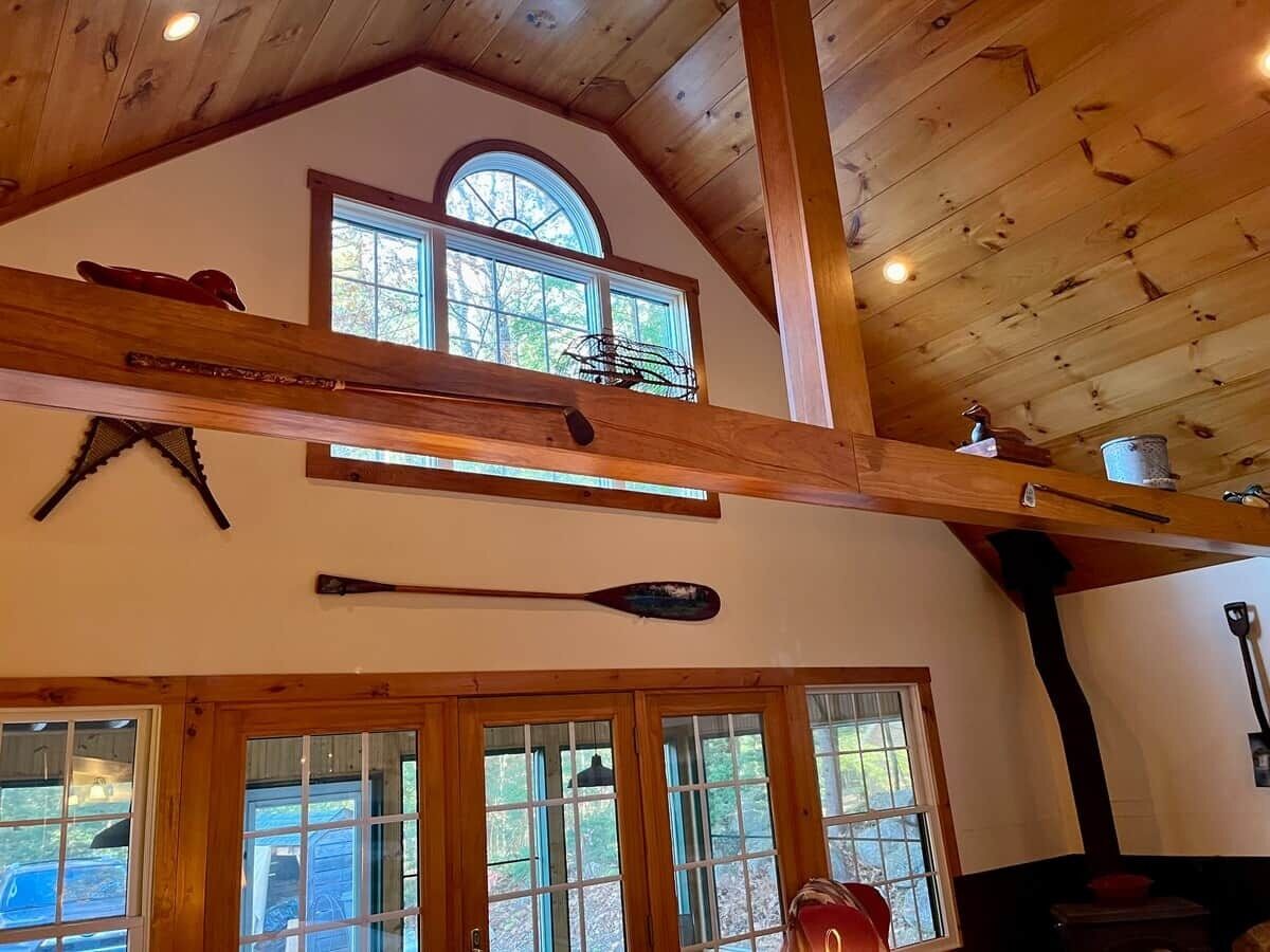 Une pièce aux hauts plafonds, avec des poutres en bois, de grandes fenêtres et un décor rustique.