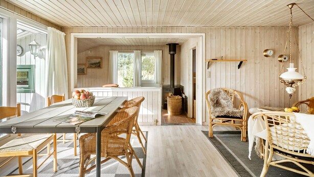 A cozy room with a wooden ceiling, a dining table with chairs, a wicker chair, a wicker basket, and a lamp. - 3 bedroom stunning home in Rødby (Rødby)