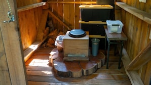 A rustic wooden cabin interior with a wooden bench, a small table, a trash bin, and a wooden ladder.