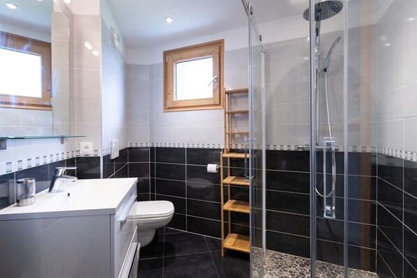 A modern bathroom with a glass-enclosed shower, a white toilet, and a black-tiled wall.