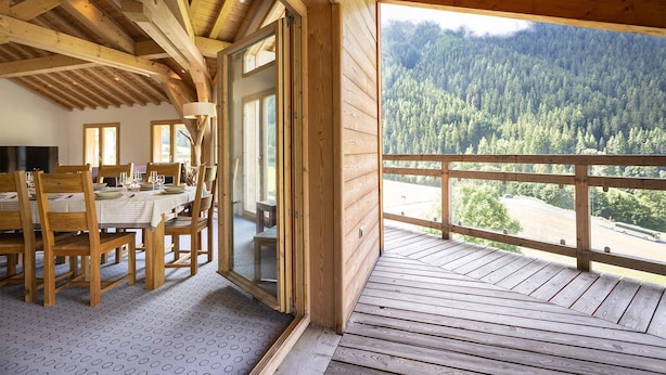 Interior de madera con comedor y balcón con vistas a una montaña boscosa.