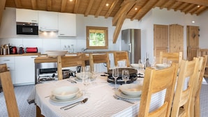 Cocina moderna con vigas de madera, armarios blancos y comedor preparado para seis personas, con la mesa lista para comer.