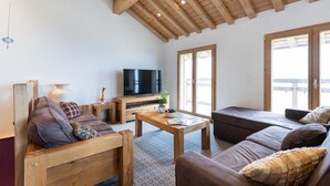 Una sala de estar acogedora con muebles de madera, televisor y ventanas amplias.