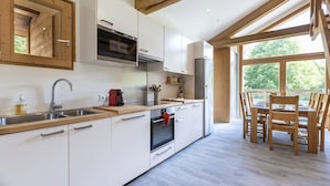 A modern kitchen with white cabinets, stainless steel appliances, and a wooden dining table with chairs. - Appt + mezzanine | Vue imprenable (Peisey-Nancroix)