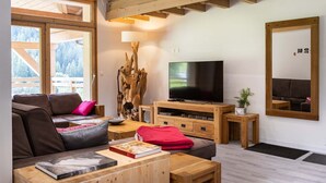 A modern living room with a wooden ceiling, a large flat-screen TV, a sofa, a coffee table, and a bookshelf. - Appt + mezzanine | Vue imprenable (Peisey-Nancroix)