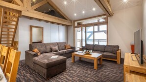 A modern living room with two sofas, a coffee table, and a TV. The room features exposed wooden beams, large windows, and a patterned floor. - Appt au calme avec vue imprenable ! (Peisey-Nancroix)