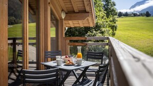Zona pranzo all'aperto con tavolo apparecchiato per la colazione, con vista su un paesaggio verdeggiante e montagne.