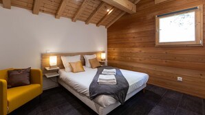 Una camera da letto con soffitto in legno, un letto con cuscini, un comodino con una lampada e una finestra.