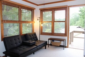 A modern living room with a black leather sofa, wooden blinds on large windows, and a small table with a basket.