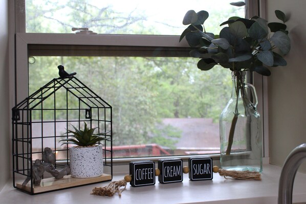 A window sill with a birdcage, a potted plant, and three labeled blocks reading "COFFEE," "CREAM," and "SUGAR."
