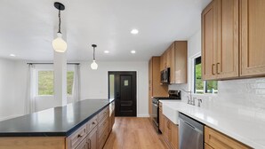 A modern kitchen with wooden cabinets, a black countertop, and stainless steel appliances. - Modern Guesthouse on 5 Acre Estate Near Wineries (Temecula)