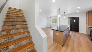 A modern kitchen with wooden flooring, a central island, and a staircase with patterned tiles. - Modern Guesthouse on 5 Acre Estate Near Wineries (Temecula)
