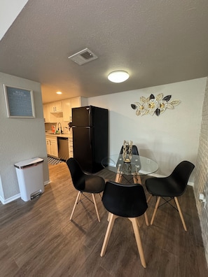 A compact kitchen with white cabinets, a black refrigerator, and a small dining area with a glass table and black chairs. - Downtown Dallas Premiere Escape 1Bed Abode (Dallas)