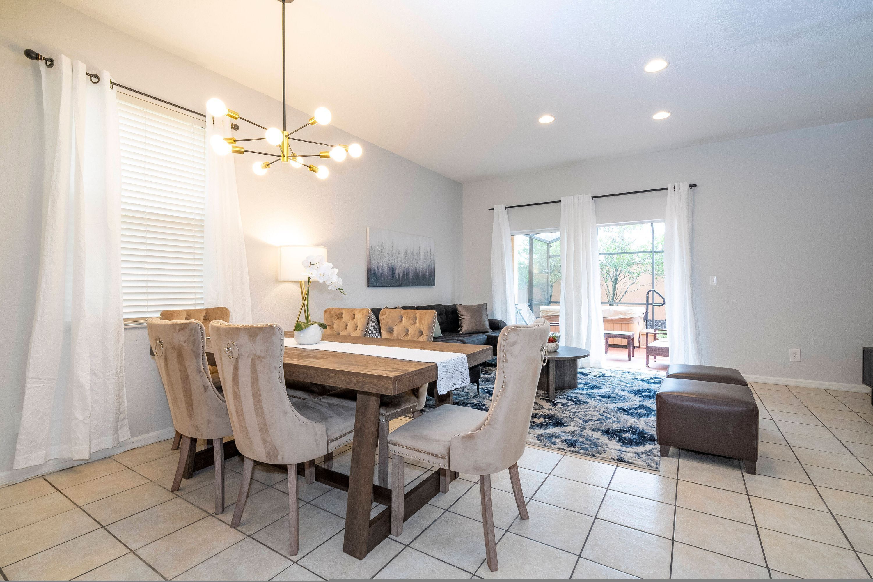 A dining area with a wooden table and chairs, a sofa, and a chandelier.