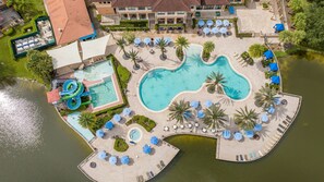 An aerial view of a resort with multiple swimming pools, a water slide, and lounge areas with umbrellas. - Cozy 4BR Regal Oaks w hot tub (Kissimmee)
