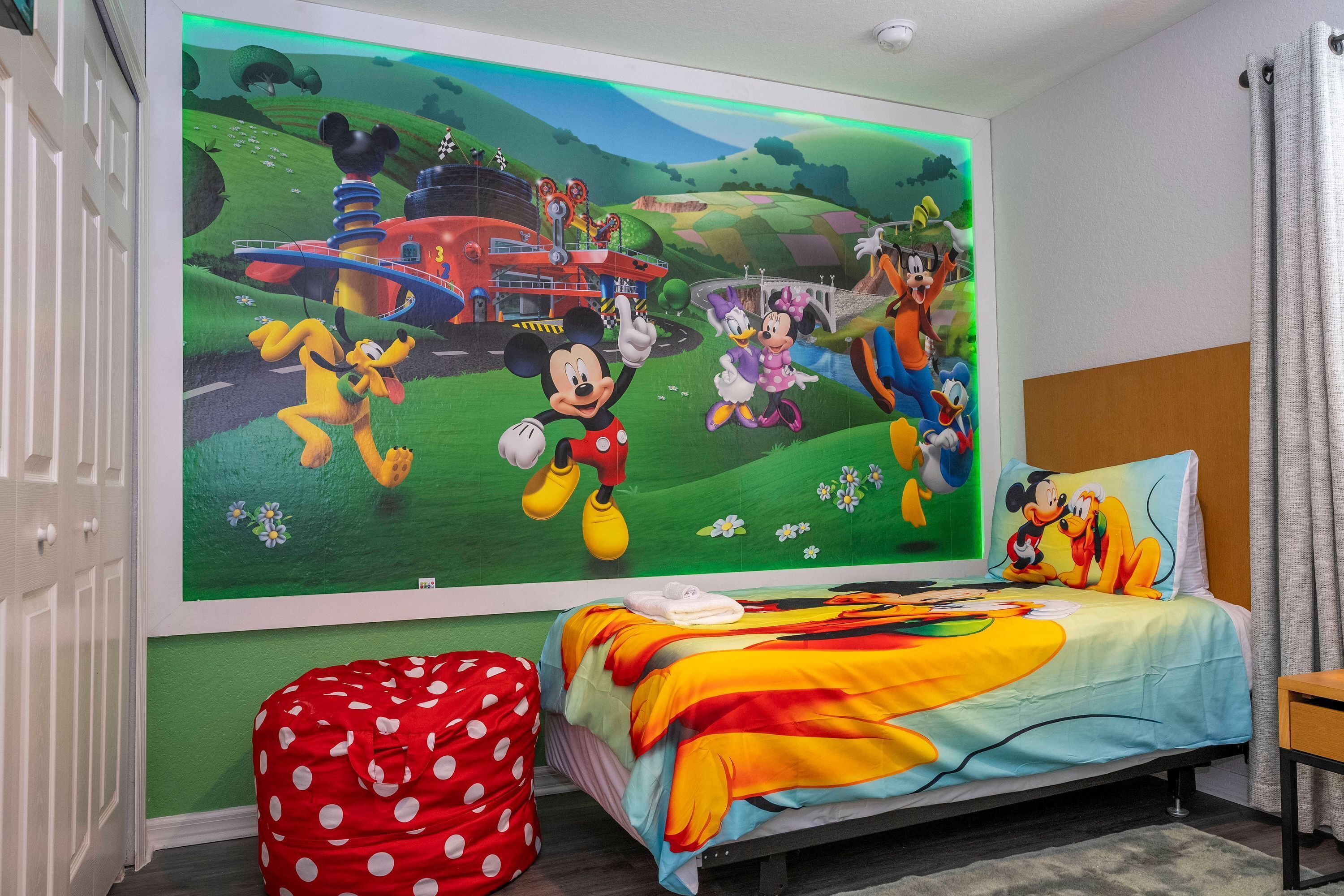 A bedroom with a large Disney-themed mural on the wall, a polka-dotted bean bag chair, and a bed with a colorful blanket.