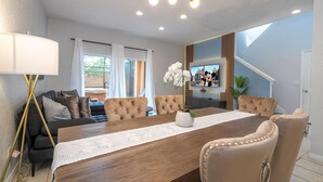 Un comedor moderno con una mesa de madera, sillas tapizadas en color beige y un jarrón blanco con flores.