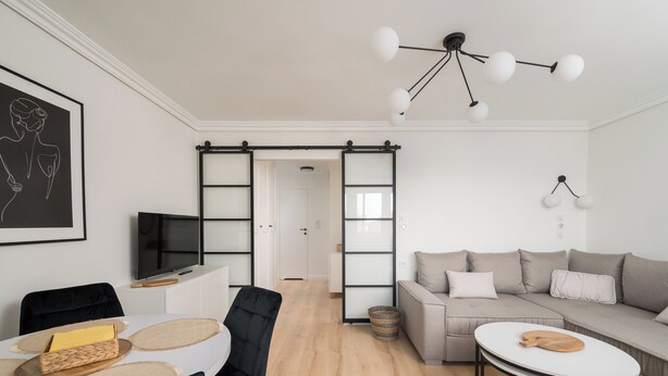 A modern living room with a sofa, a dining table with chairs, a TV, and a unique ceiling light fixture. - Aleja Waszyngtona Deluxe Apartment (Warszawa)