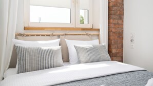 A neatly made bed with striped pillows, a wooden headboard, and a window with white curtains. - Aleja Waszyngtona Deluxe Apartment (Warszawa)