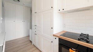 A modern kitchen with white cabinetry, a black stove, and a wooden countertop. - Aleja Waszyngtona Deluxe Apartment (Warszawa)