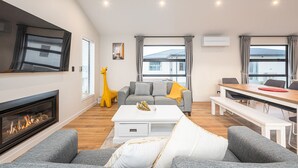 Una sala de estar moderna con chimenea, sofás grises, una mesa de comedor y un ventanal grande.