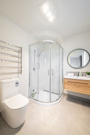 Ein modernes Badezimmer mit Duschkabine, Toilette, Waschbecken mit Spiegel und Handtuchhalter.