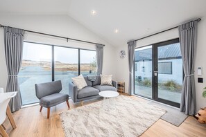 A modern living room with a grey sofa, two armchairs, a small white coffee table, and a large window with grey curtains.