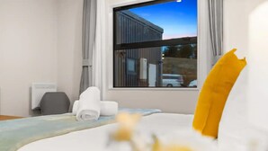 Een hotelkamer met een bed, een raam met uitzicht op een gebouw, een stoel en een bureau met een computer.