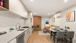 Een moderne keuken met een inbouwvaatwasser, een gasfornuis en een spoelbak. Er is een eethoek met een tafel gedekt voor vier personen, en een bankstel op de achtergrond.
