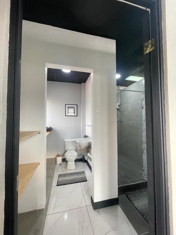 A modern bathroom with a toilet, sink, and shower area. - San José Downtown Suites  (San José)