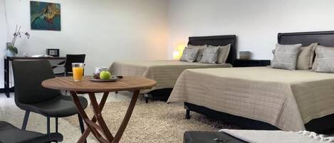 Habitación de hotel con dos camas, una mesita con una bebida y fruta, una silla y un escritorio con una lámpara.