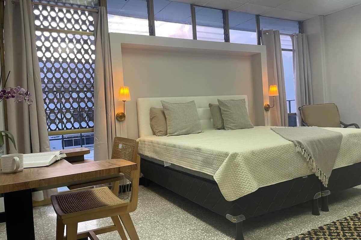 Una camera d'albergo con un letto, due comodini, una scrivania, una sedia e una finestra con vista.