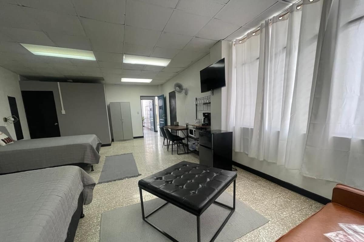 Camera d'albergo con due letti, un tavolino, una scrivania con una sedia, una televisione e una finestra con tende.