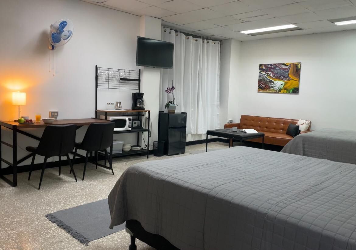 A hotel room with a bed, a desk with chairs, a television, a coffee machine, and a painting on the wall.