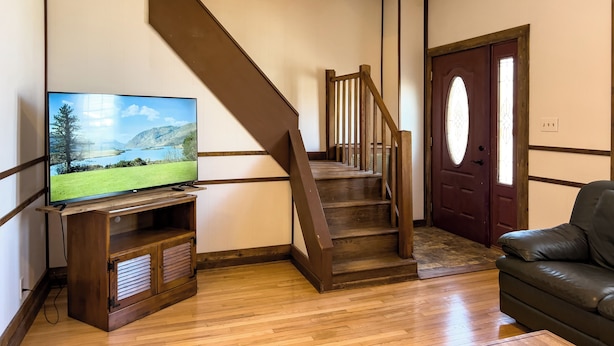 A living room with a wooden staircase, a television on a wooden stand, and a leather sofa. - Charming, historic 3-bedroom house in quaint Fredericksburg with AC, WiFi (Fredericksburg)