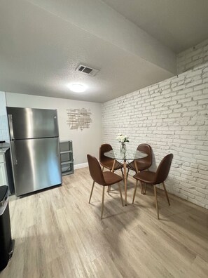 A modern kitchen with a stainless steel refrigerator, a dining table with four brown chairs, and a white brick wall. - DT Dallas LUXE Urban Oasis 1BD Apt (Dallas)