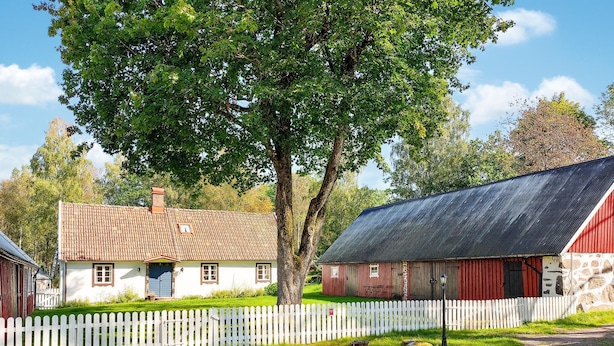 A rural setting with a white picket fence, a red barn, and a white house with a tiled roof.