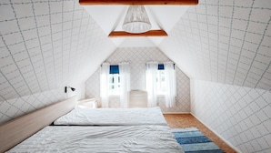 A bedroom with a sloped ceiling, a wooden beam, a bed, a nightstand, a lamp, and a window with curtains.