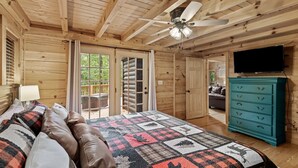 Un dormitorio de cabaña de madera con una cama, un aparador azul turquesa, un ventilador de techo y un televisor.