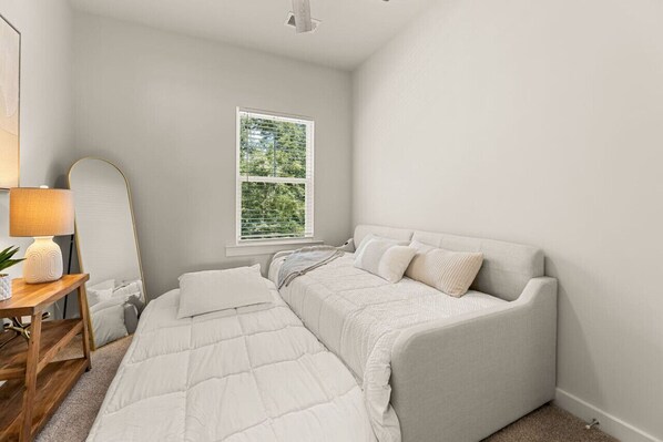 A bedroom with a bed, bedside table, lamp, and window. - Lux Charleston Residence for 10+ (Hanahan)