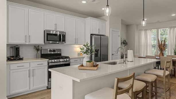 A modern kitchen with white cabinetry, stainless steel appliances, a central island with bar stools, and pendant lighting. - Lux Charleston Residence for 10+ (Hanahan)